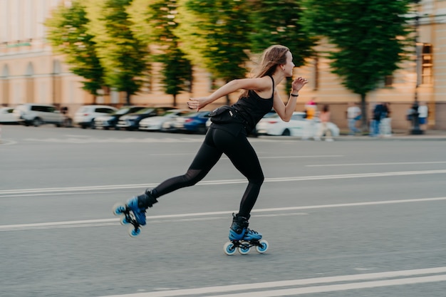 Professionelle weibliche Roller demonstriert ihre Fähigkeiten von Rollerblading-Fahrten sehr schnell auf der Straße entlang der Stadt genießt einen sonnigen Tag in schwarzer aktiver Kleidung. Aktives Lifestyle-Hobby und Fitness-Aktivität