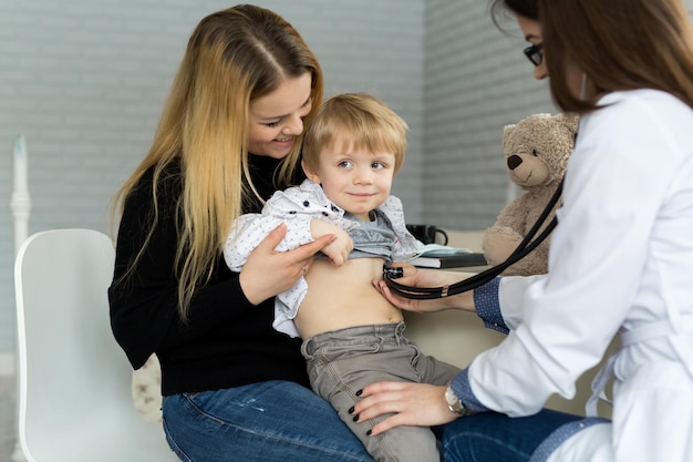 Professioneller allgemeinmedizinischer Kinderarzt in weißem Uniformkleid hört Lungen- und Herzgeräusche