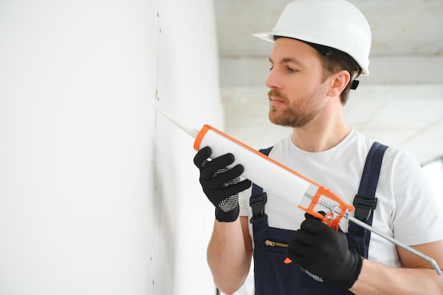 Professioneller Arbeiter, der Silikondichtmittel mit Kartuschenpistole an der Wand aufträgt