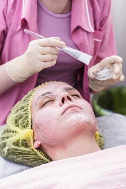Professioneller Arzt trägt eine kosmetische Maske mit einem Pinsel auf das Gesicht einer Frau auf, Nahaufnahme.