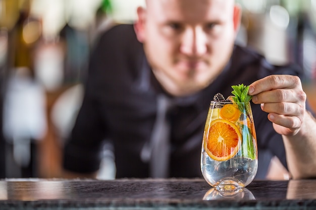 Professioneller barmann, der gin-tonic-cocktail-getränk dekoriert und mit minzkräutern dekoriert.