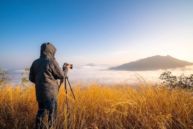 professioneller fotograf, der ein foto mit kameraobjektiv auf stativ mit bergsonnenuntergangblick macht
