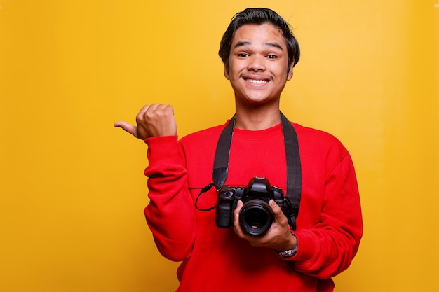 Professioneller Fotograf lächelt und hält die Kamera, während er mit dem Finger zur Seite zeigt
