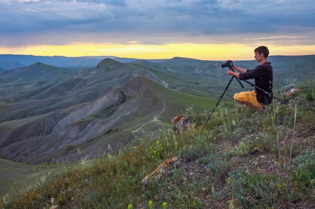 Professioneller Fotograf mit Stativ, der eine Berglandschaft bei Sonnenuntergang fotografiert photo