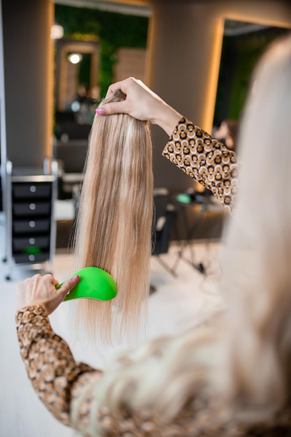 Professioneller Friseur bereitet blondes Haar für Verlängerungen vor und kämmt sie in einem Schönheitssalon