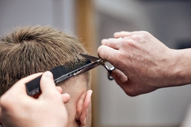 Professioneller Friseur, der dem jungen Mann mit Schere und Kamm im Friseursalon Haarschnitt macht