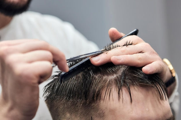 Professioneller Friseur, der dem jungen Mann mit Schere und Kamm im Friseursalon Haarschnitt macht