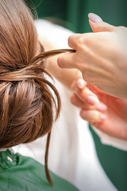 Professioneller Friseur, der Frisur für eine schöne brünette junge Frau mit langen Haaren macht. Konzept von Mode und Schönheit.