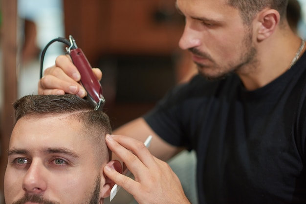 Professioneller Friseur, der mit einem Haarschneider arbeitet, der Haare seines Kunden stylt