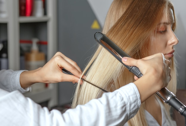 professioneller Friseur glättet das Haar mit Stylingeisen