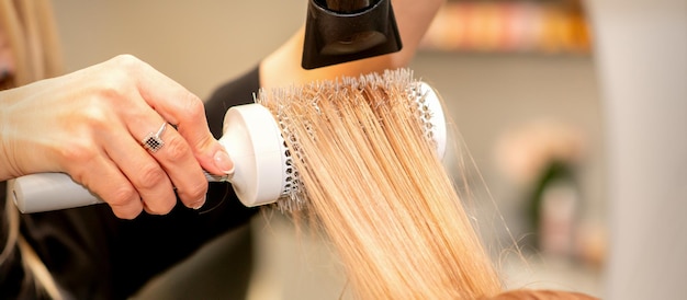 Professioneller Friseur trocknet Haare mit einem Haartrockner und einer runden Haarbürste in einem Schönheitssalon.