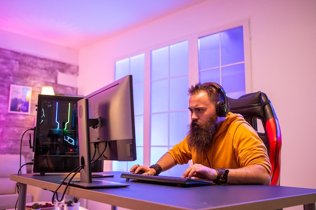 Professioneller Gamer mit langem Bart vor einem leistungsstarken Gaming-Rig in einem Raum voller Neonlichter