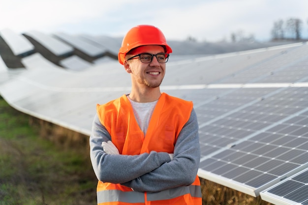 Professioneller Ingenieur in orangefarbener Uniform posiert an der Fotokamera in der Nähe des Energiebauernhofs