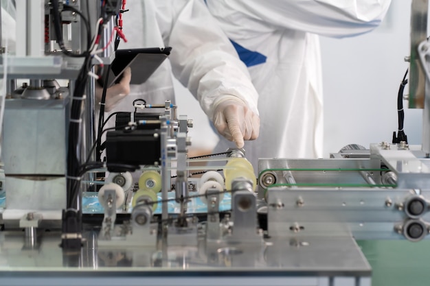 Professioneller Ingenieur in sterilen Tüchern und Gesichtsmasken, die Maschine in der Fabrik für chirurgische Masken arbeiten und kontrollieren. Industriefabrik und Menschenkonzept. drinnen