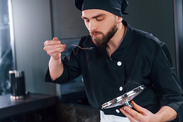 Professioneller junger Koch in Uniform, der an der Küche arbeitet