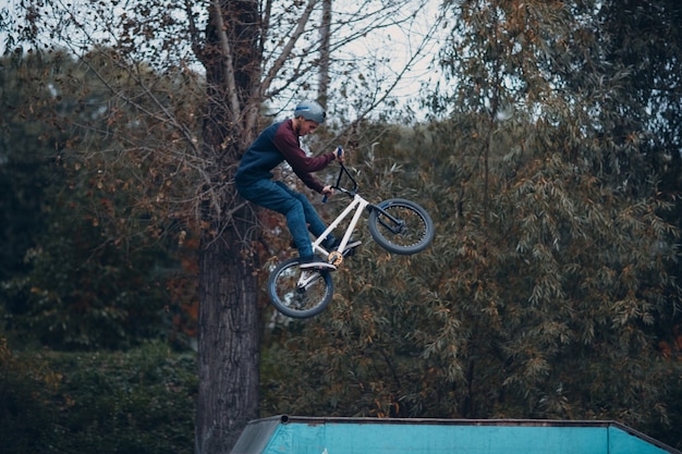 Professioneller junger Sportler-Radfahrer mit BMX-Fahrrad, der Trick im Skatepark macht