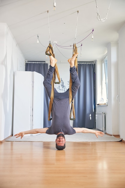 Professioneller kaukasischer dunkelhaariger bärtiger Yogi, der einen Kopfstand mit einer Seidenhängematte in einem Fitned übt