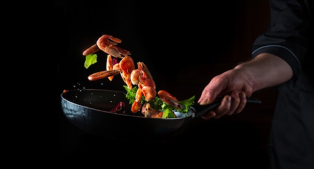 Professioneller Koch bereitet Garnelen mit Kräutern zu. Kochen von Meeresfrüchten, gesundem vegetarischem Essen und Essen auf dunklem Hintergrund. Kostenlose Werbefläche