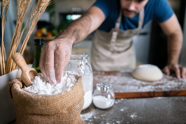 Professioneller Koch drescht weißes Mehlpulver auf Holztisch für süßen Dessertkuchen und italienische Pizza in der Restaurantküche für ein besonderes, fröhliches, köstliches Abendessen