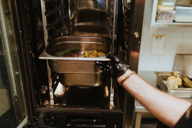 Professioneller Koch in der Restaurantküche, der köstliche Mahlzeiten mit Fleisch und Gemüse zubereitet.