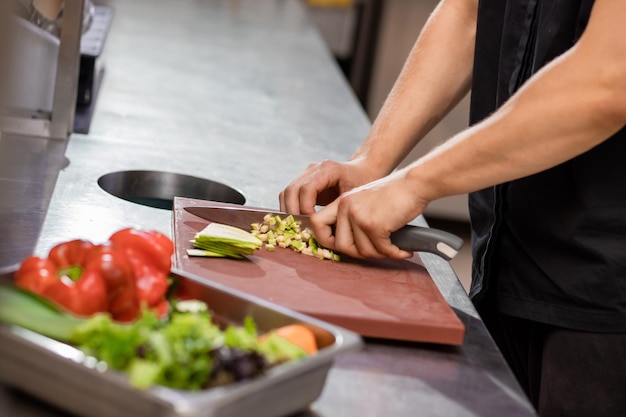 Professioneller Koch in Uniform bereitet frisches Gemüse auf Schneidebrett in der Restaurantküche zu Kulinarisches Konzept