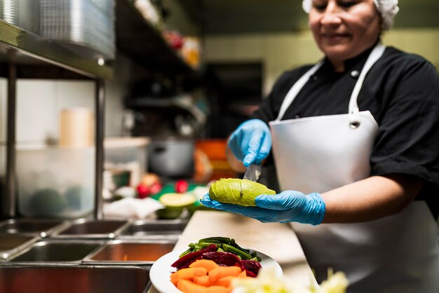 Professioneller Koch in Uniform, der Gemüse über seiner Hand mit einer Vielzahl von Gemüse auf dem Tisch in der Küche des Restaurants schneidet