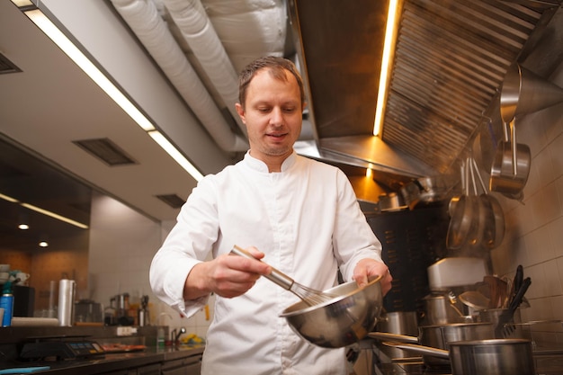 Professioneller Koch lächelt, verquirlt Sauce in einer Schüssel und genießt die Arbeit in seinem Restaurant