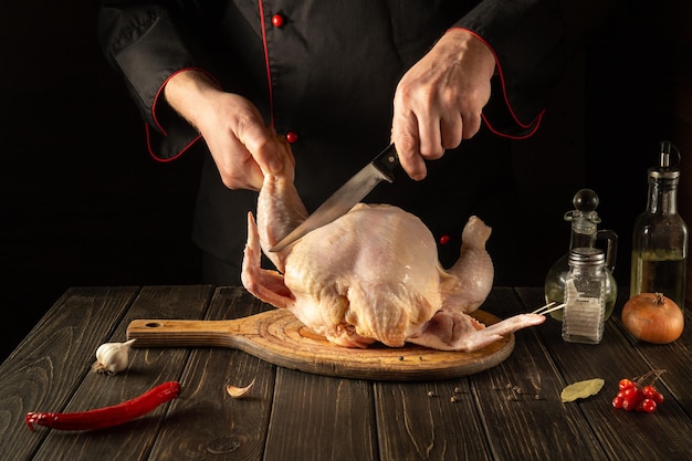 Professioneller Koch schneidet rohes Huhn mit einem Messer in der Küche