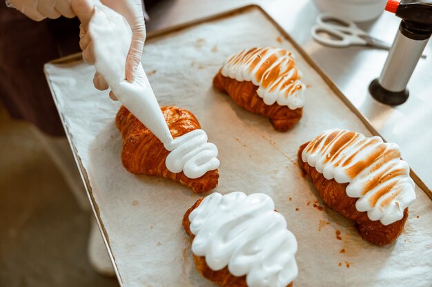 Professioneller Konditor trägt in der Bäckerei süße Sahne auf Croissants aus der Tüte auf