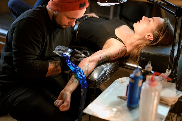 Professioneller männlicher bärtiger kaukasischer Tattoo-Meister arbeitet in einem gemütlichen atmosphärischen Studio