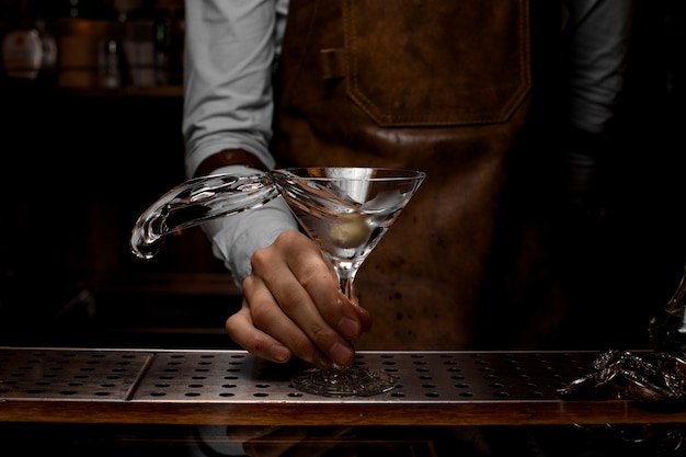 Professioneller männlicher Barmixer, der ein transparentes alkoholisches Getränk im Martini-Glas mit einer Olive mischt