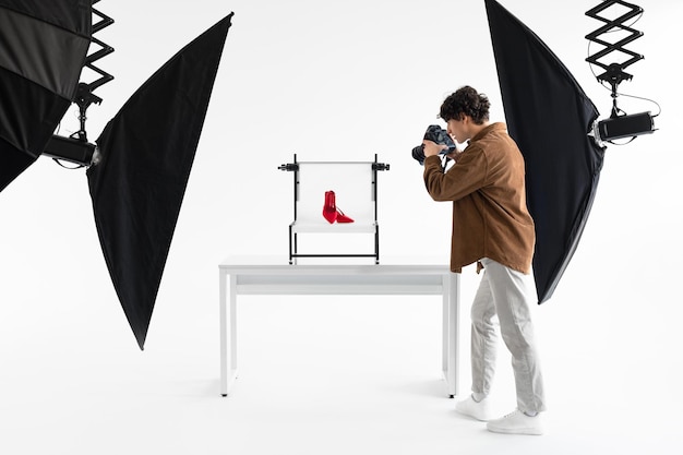 Foto professioneller männlicher content-maker, der fotos von eleganten roten schuhen macht, die in einem modernen fotostudio arbeiten