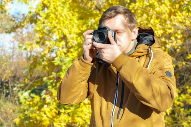 Professioneller männlicher fotograf, der draußen im gelben wald des herbstes auf moderner dslr-kamera schießt. leerer bereich mit kopierraum für text.
