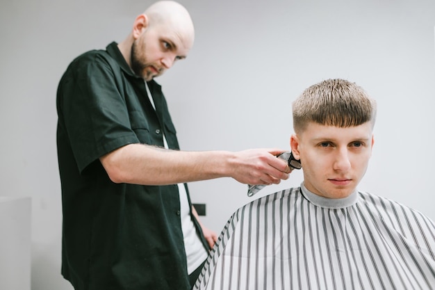 Professioneller männlicher Friseur kreiert eine modische Frisur für einen hübschen jungen Mann an der Wand