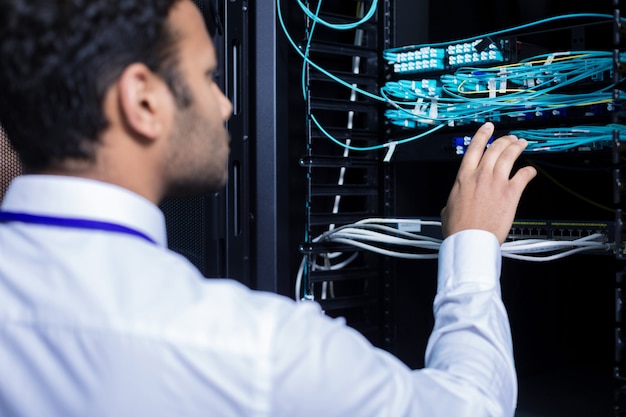 Professioneller männlicher IT-Administrator, der vor dem Netzwerkserver steht und die Internetkabel überprüft, während er seine Arbeit erledigt