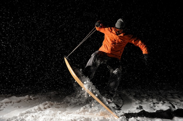 Professioneller männlicher Snowboarder, der auf Schnee nachts springt