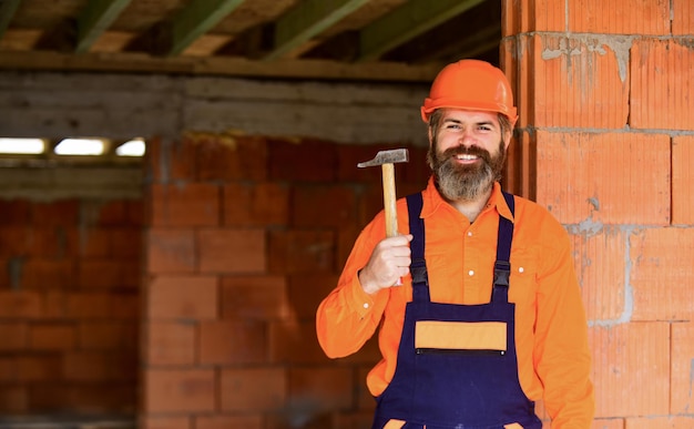 Foto professioneller mechaniker verwendet hammerbau und -konstruktion qualifizierter architekt repariert und repariert ingenieurkarriere reifer bärtiger mann mit hartem hut baumeister in einem unfertigen gebäude