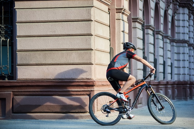 Professioneller Radfahrer, der Fahrrad im Stadtzentrum rast und Gebäude vorbeifährt. Sportler trainieren, im Freien trainieren. Konzept des gesunden Lebensstils