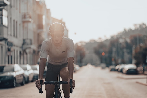 Professioneller Radfahrer mit Schutzhelm und verspiegelter Brille, der morgens auf der Stadtstraße Fahrrad fährt Konzept von Menschen und Training