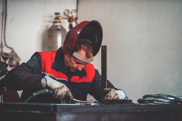 Professioneller Schweißer in Schutzuniform und Maskenschweißen von Metallrohren auf dem Industrietisch mit ot