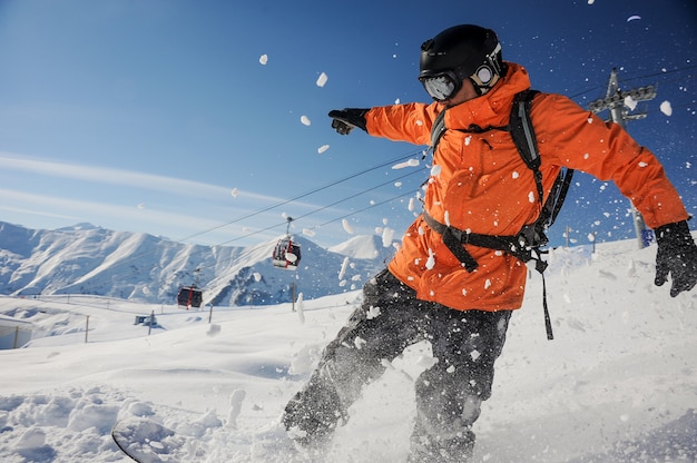 Professioneller Snowboarder in orangefarbener Sportbekleidung, der einen Berghang hinunter fährt