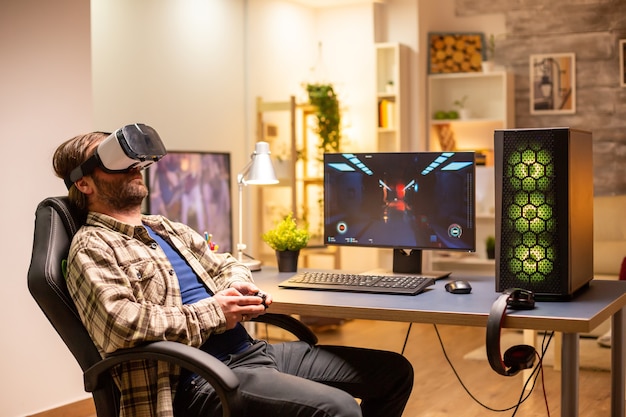 Professioneller Spieler mit VR-Headset, um spät in der Nacht in seinem Wohnzimmer auf einem leistungsstarken PC zu spielen