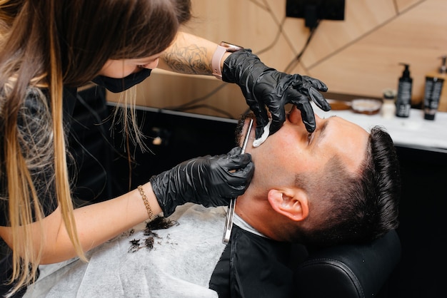 Professioneller Stylist in einem modernen, stilvollen Friseurladen rasiert und schneidet einem jungen Mann die Haare