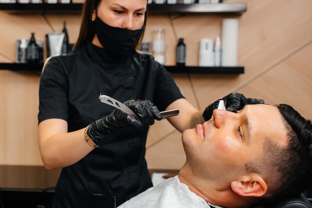 Professioneller Stylist in einem modernen, stilvollen Friseurladen rasiert und schneidet einem jungen Mann die Haare