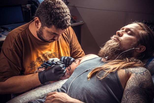 Professioneller Tätowierer bei der Arbeit im Salon./Tätowierer erstellen Tätowierungen im Tätowiersalon.