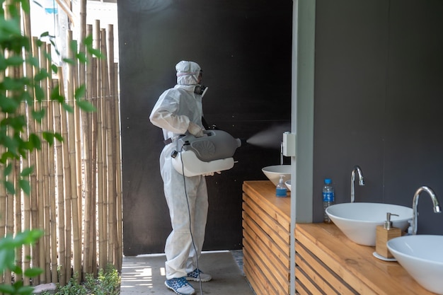 Foto professioneller techniker im präventionsanzug mit seiner sterilisationsmaschine und desinfizierenden wassersprays im toiletten- oder wc-bereich zur reinigung von coronavirus covid19