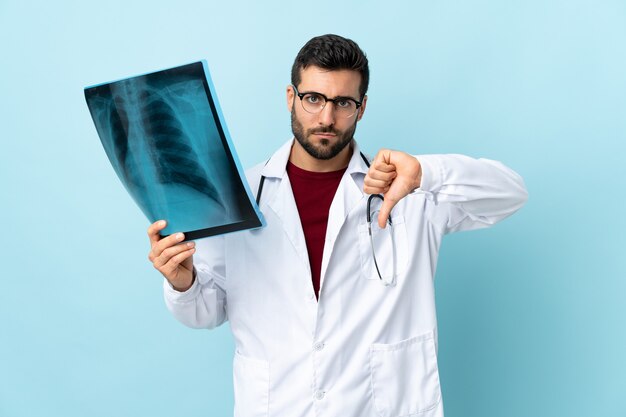 Professioneller Traumatologe, der Radiographie lokalisiert auf Blau hält, das Daumen unten Zeichen zeigt