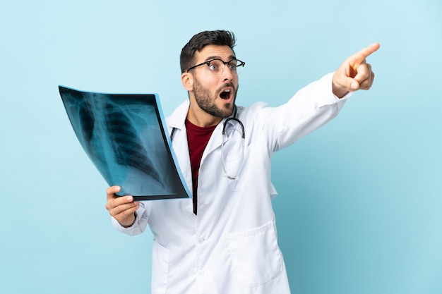 Professioneller Traumatologe, der Radiographie lokalisiert auf blauem Hintergrund hält weg zeigt