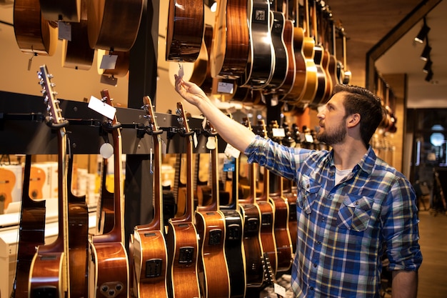 Professioneller Verkäufer, der im Musikladen steht und die Preise der zum Verkauf stehenden Gitarren überprüft.