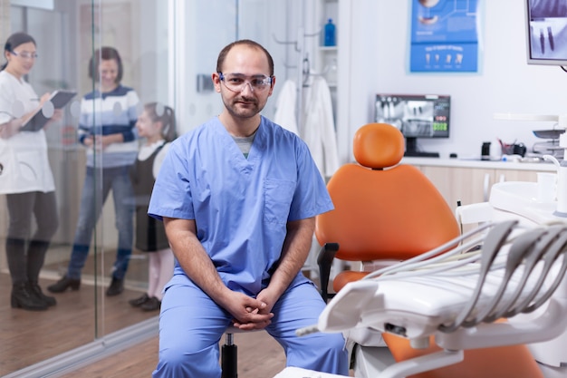 Professioneller Zahnarzt mit Schutz und Patientendiskussion mit Kieferorthopäden. Brille Stomatolog in professioanl Zahnklinik lächelnd in Uniform mit Blick in die Kamera.